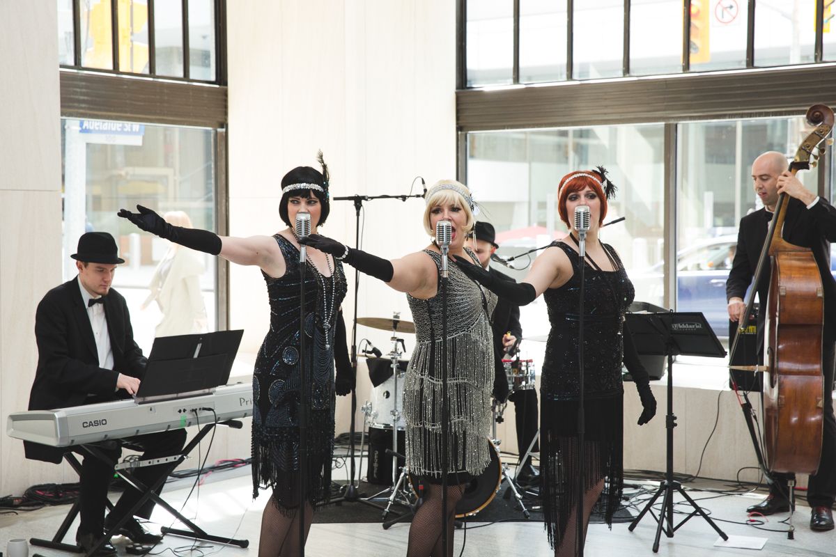 A group of women are singing into microphones while a man plays a keyboard.