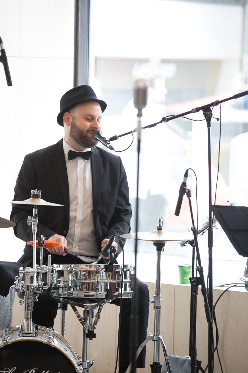 A man in a suit is playing drums and singing into a microphone.