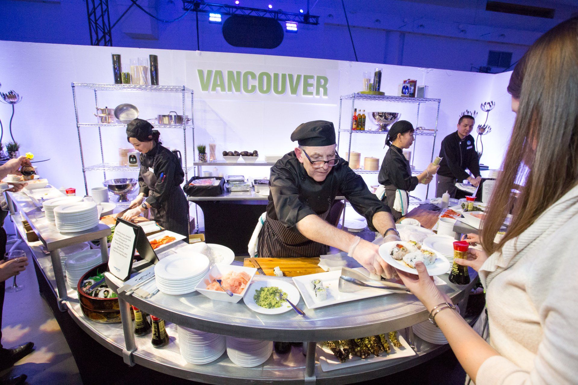 A woman is holding a plate of food in front of a sign that says vancouver