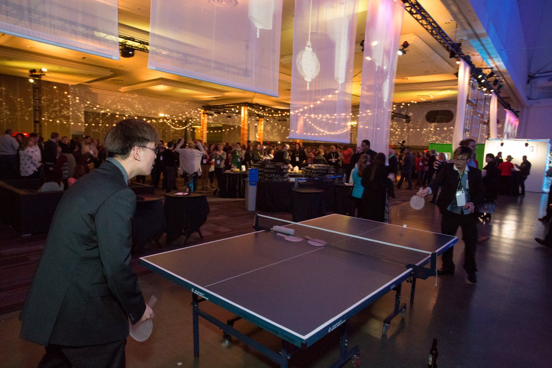 A man in a suit is playing ping pong in a large room.