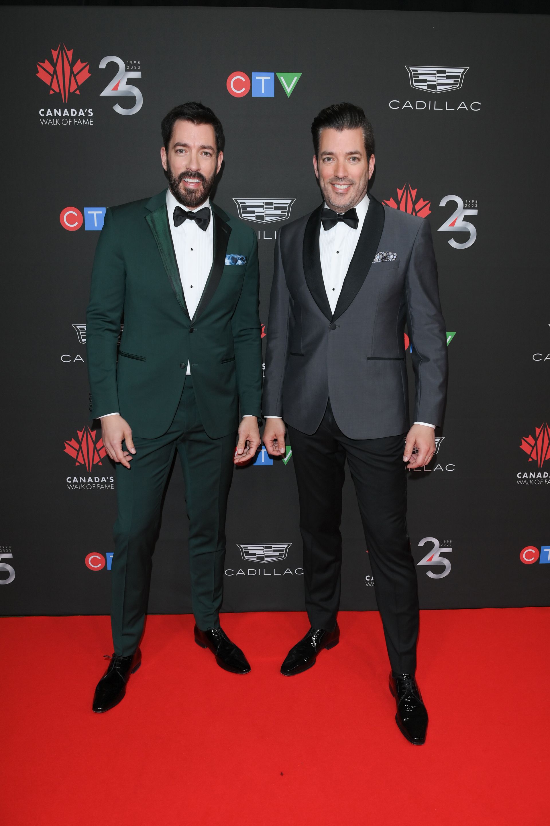 Two men in tuxedos are standing next to each other on a red carpet.