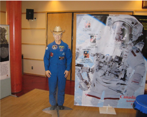 A man in a cowboy hat stands in front of a cardboard cutout of an astronaut