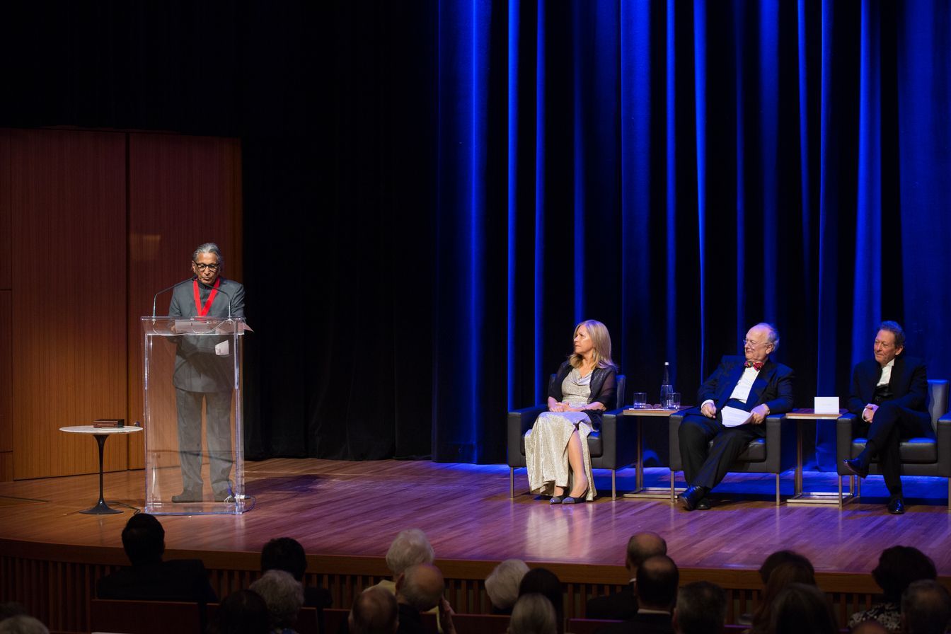 A man is standing at a podium on a stage giving a speech to a group of people sitting in chairs.