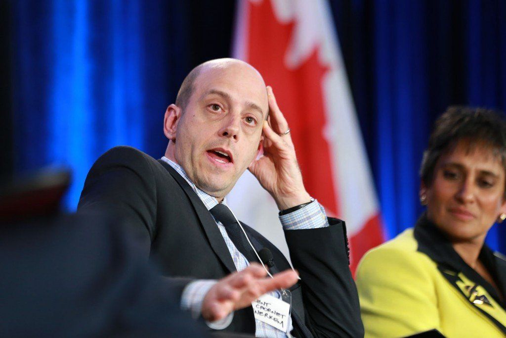 A man in a suit and tie is sitting in front of a canadian flag