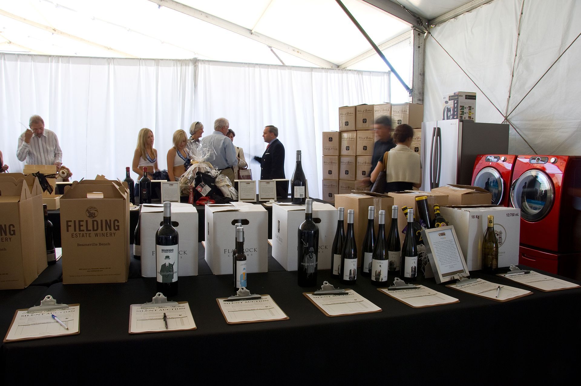 Wine tasting event with bottles, boxes, and people near a tent.
