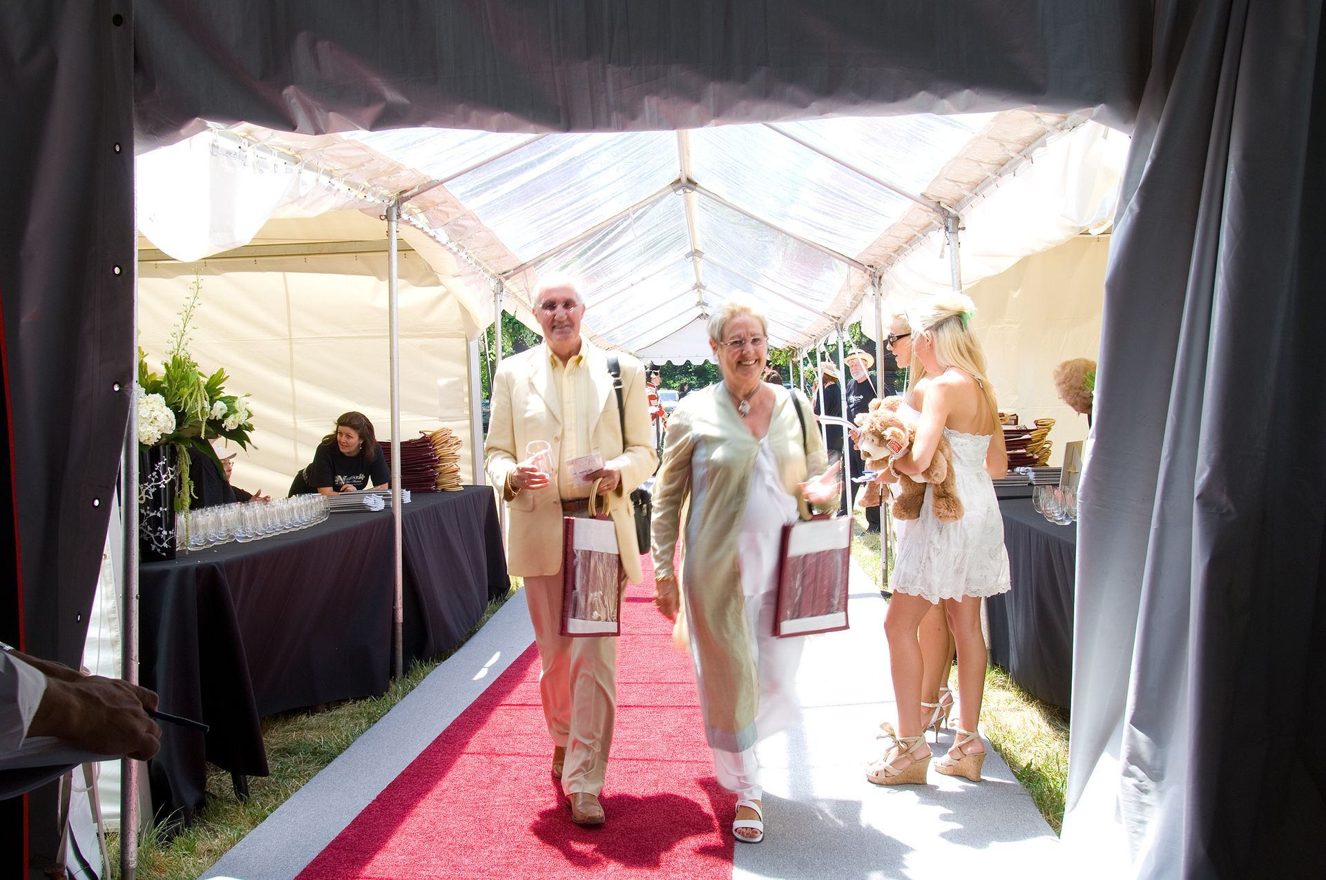 People walking down a red carpet through a tent, carrying gifts.