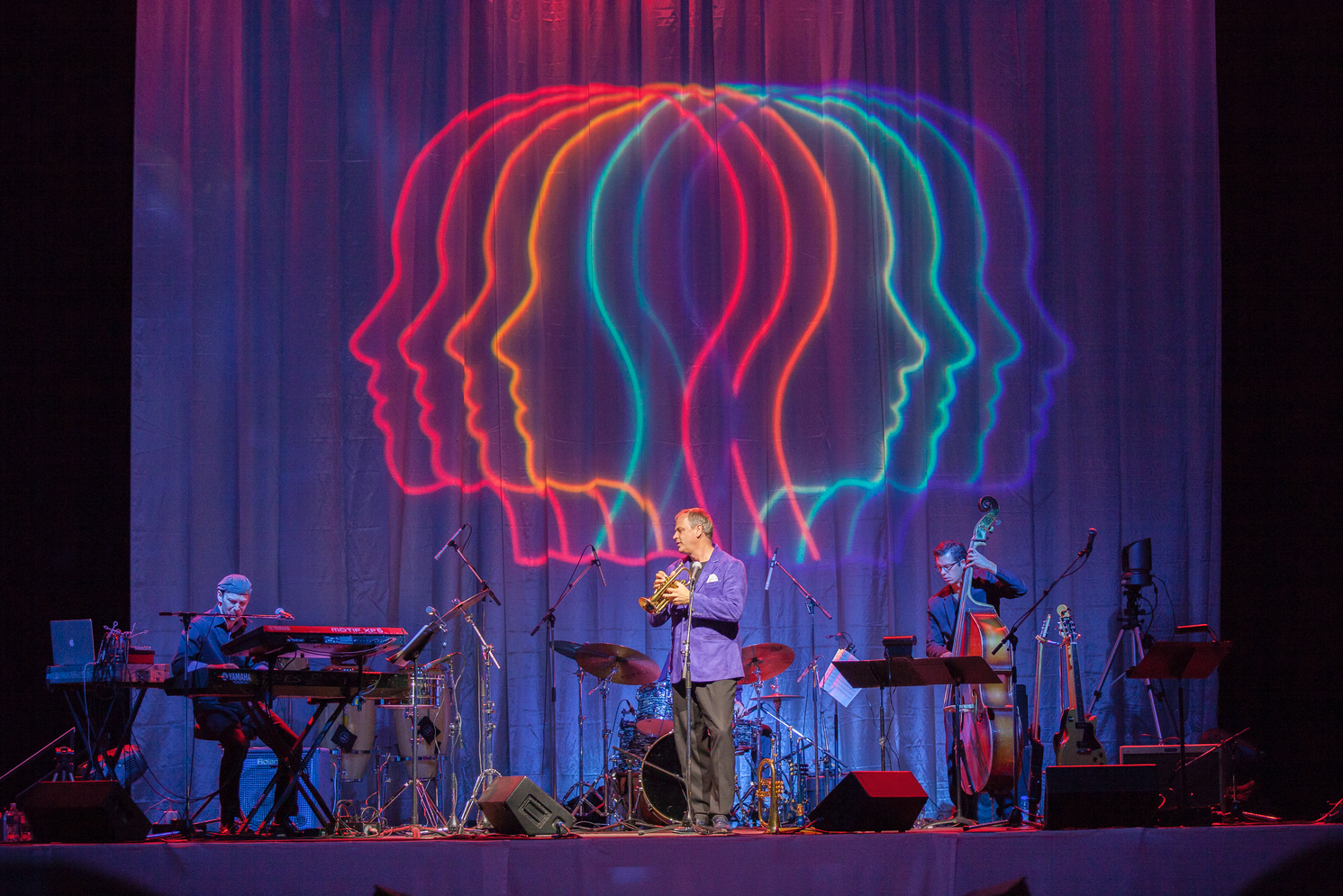 A man playing a trumpet on a stage with a rainbow colored background