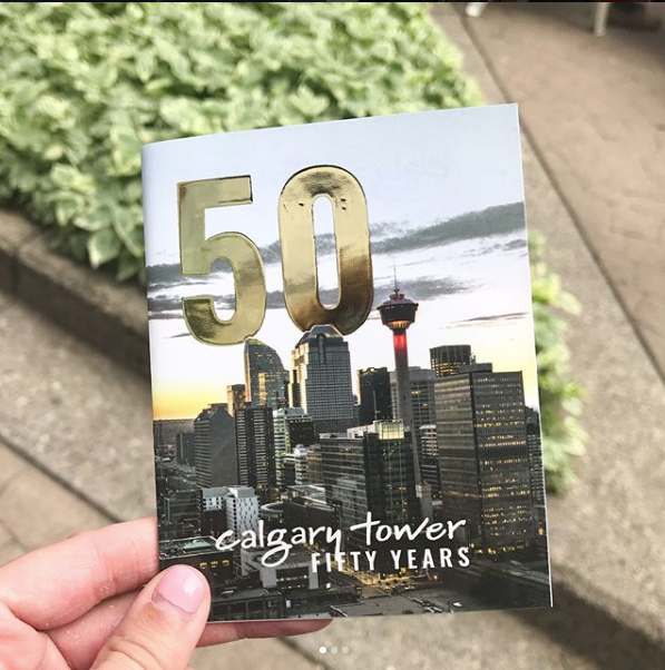 A person is holding a book titled calgary tower fifty years