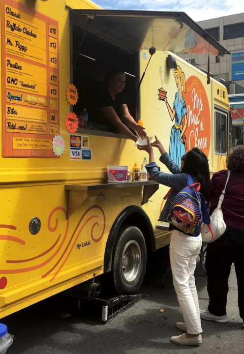 A woman is getting food from a yellow food truck