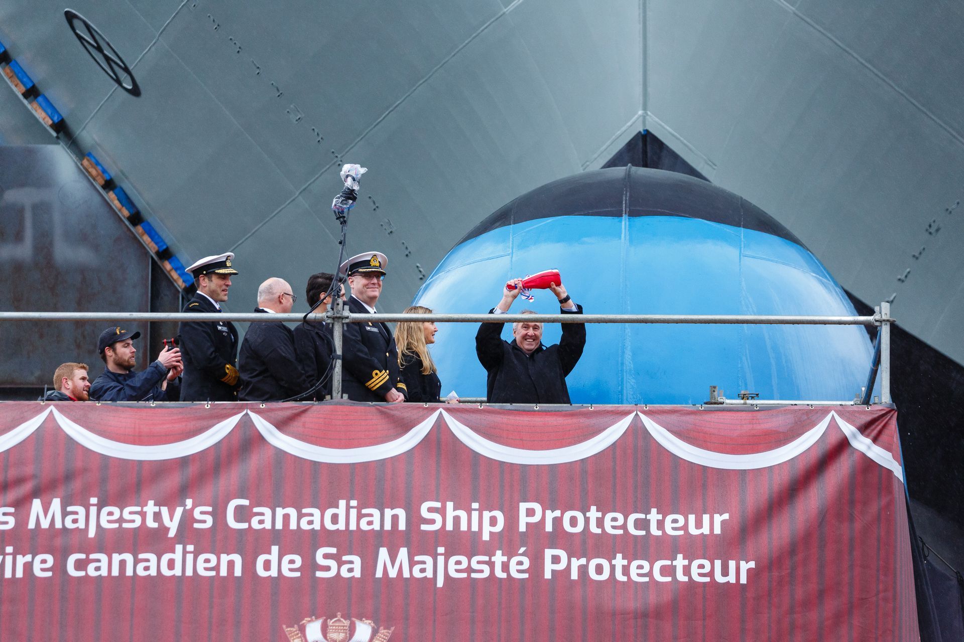 A group of people are standing in front of a banner that says ' canadian ship protector ' on it.