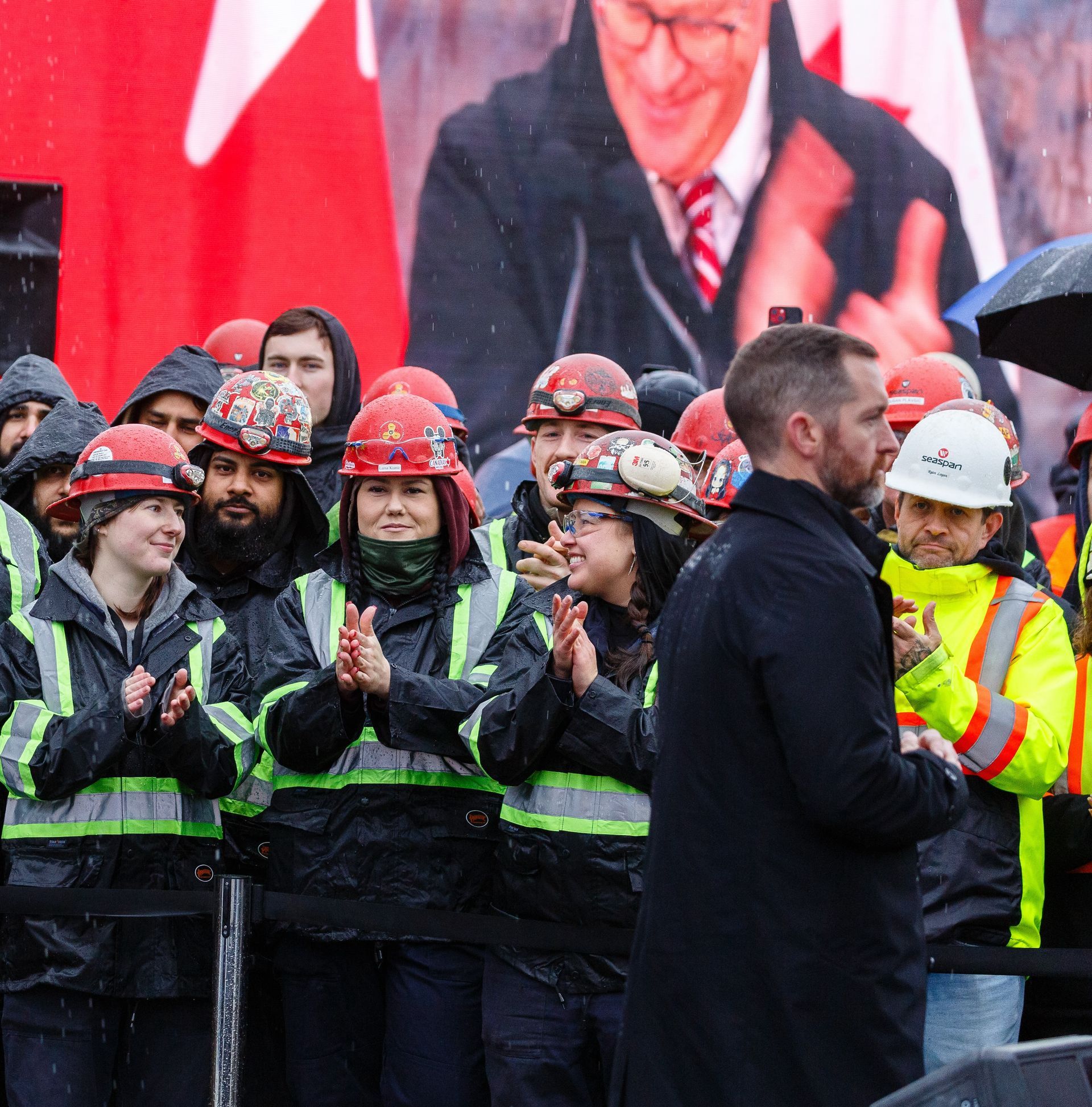 A group of people wearing hard hats are standing in front of a large picture of a man