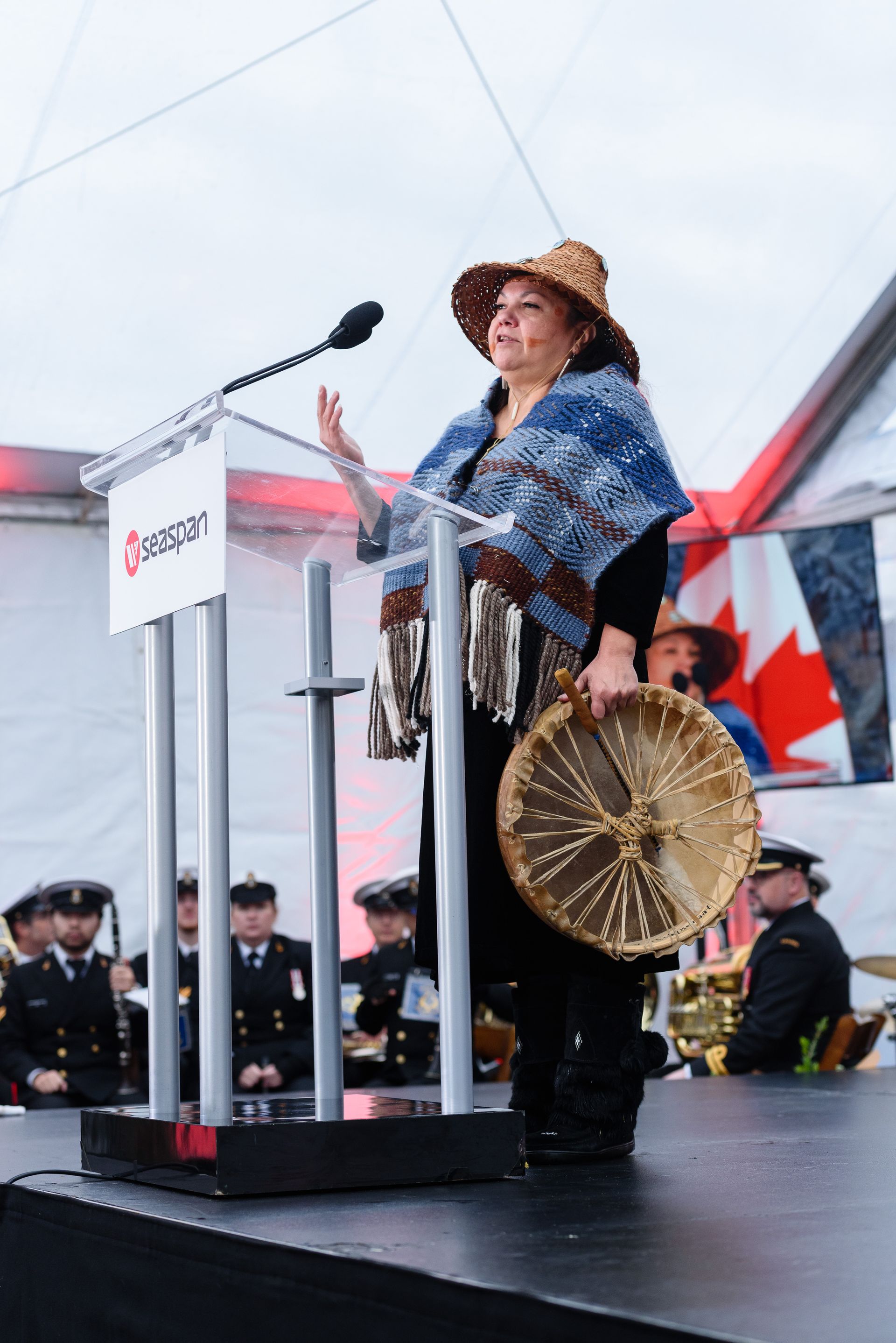 A woman is standing at a podium holding a drum.