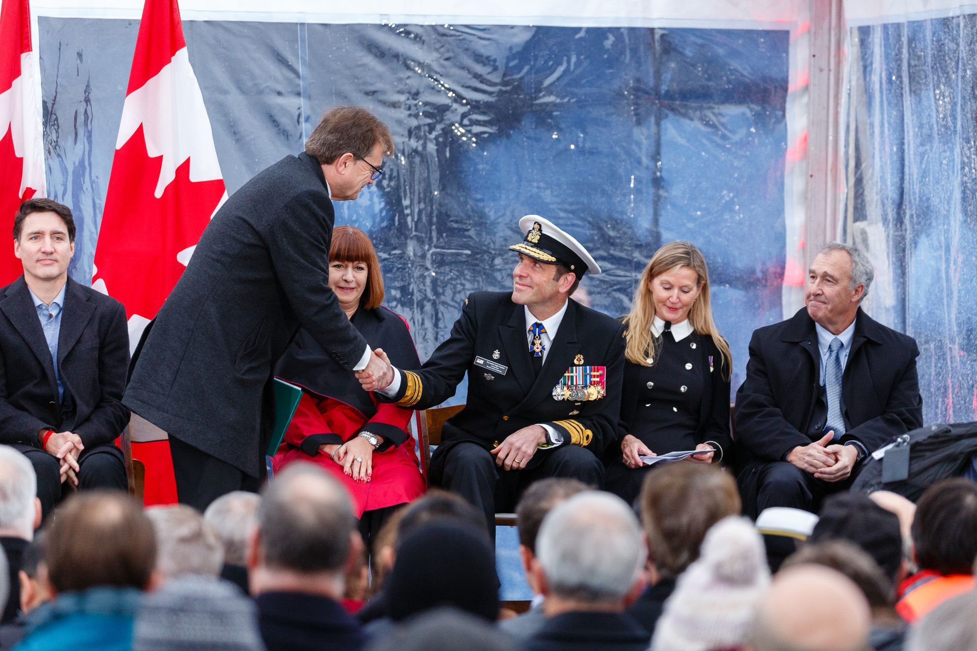 A man in a military uniform shakes hands with another man in front of a crowd.