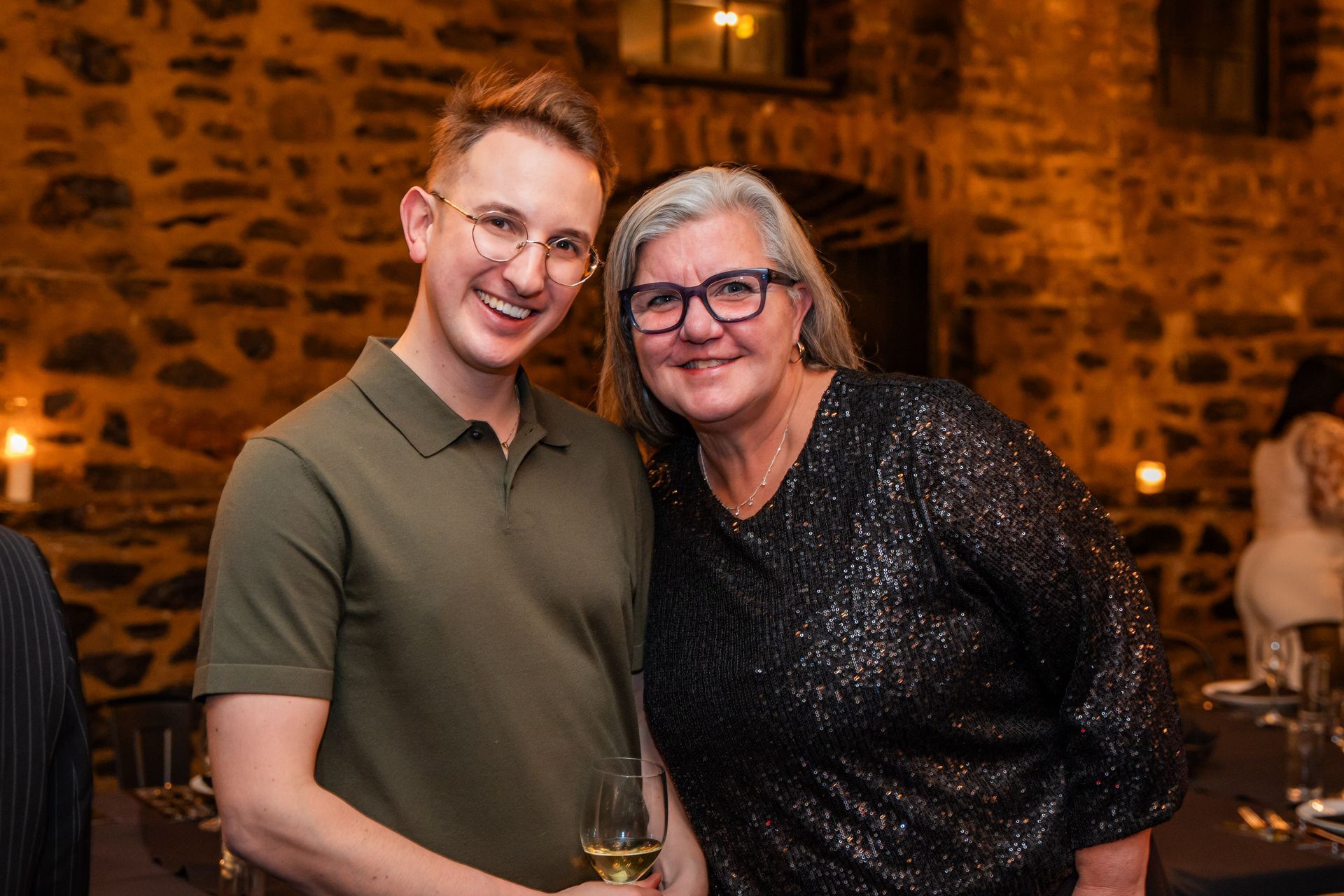 A man and a woman are posing for a picture together . the woman is holding a glass of wine.