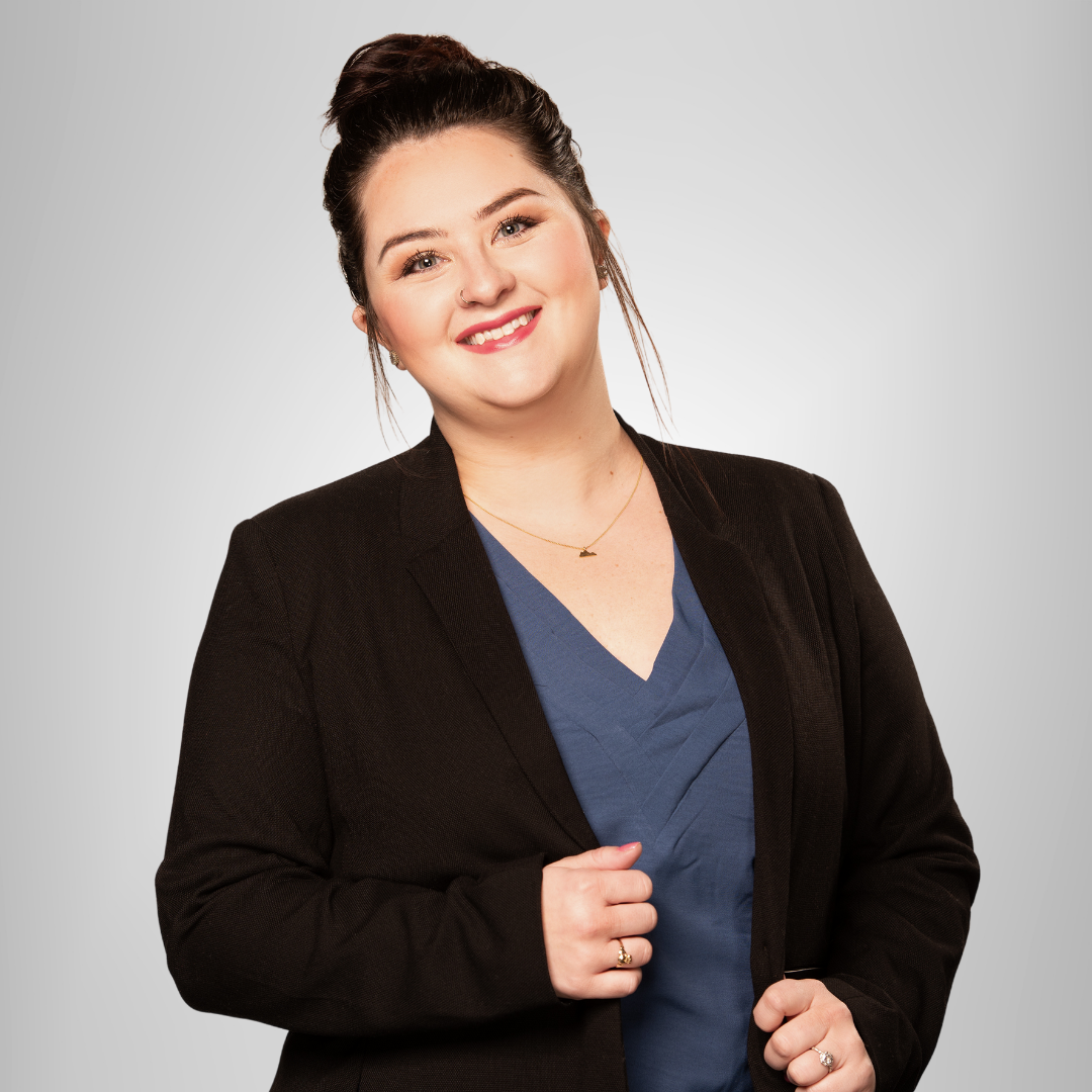 A woman wearing a black jacket and a blue shirt smiles for the camera