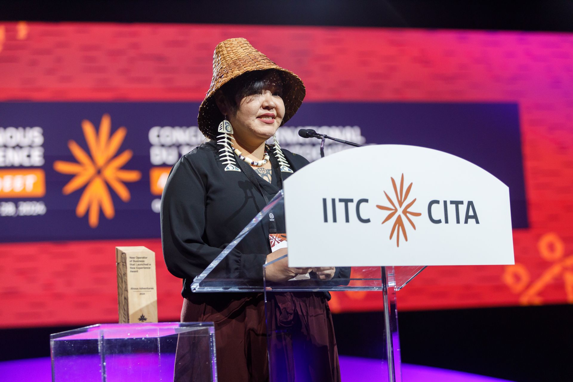 Woman in traditional hat speaking at a conference podium with logos.