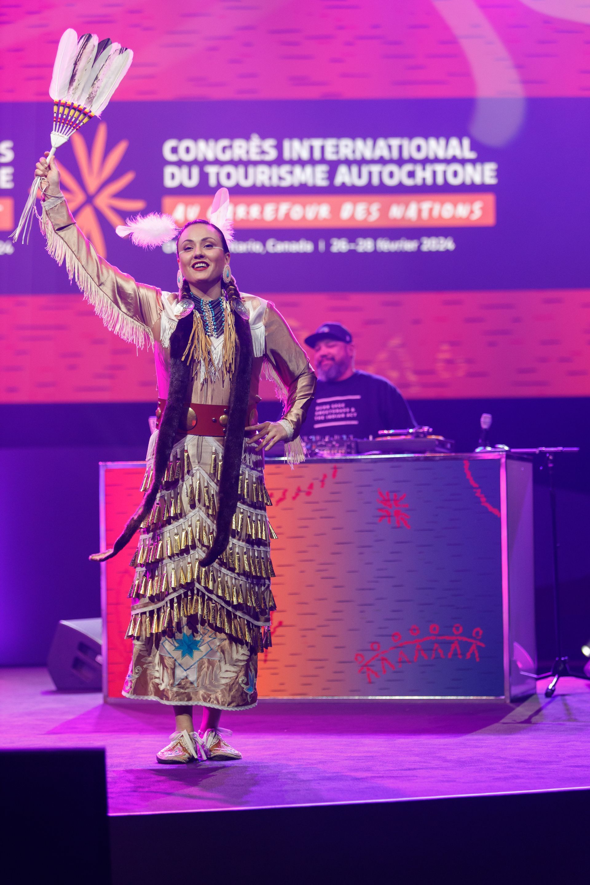 Indigenous dancer with feathered fan performing on stage at tourism congress.
