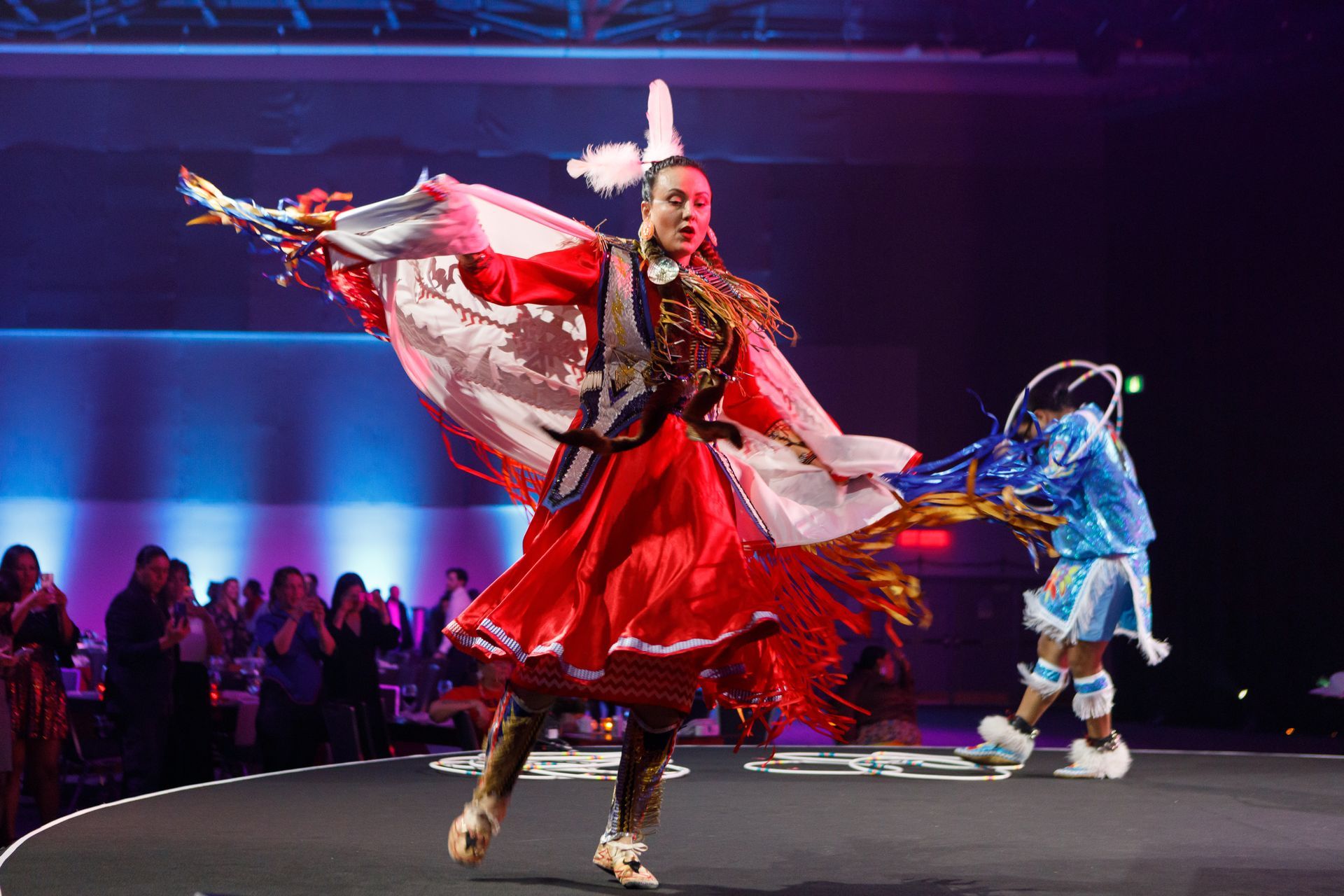 Woman dancing on stage in red dress and shawl, with a person in blue costume nearby.