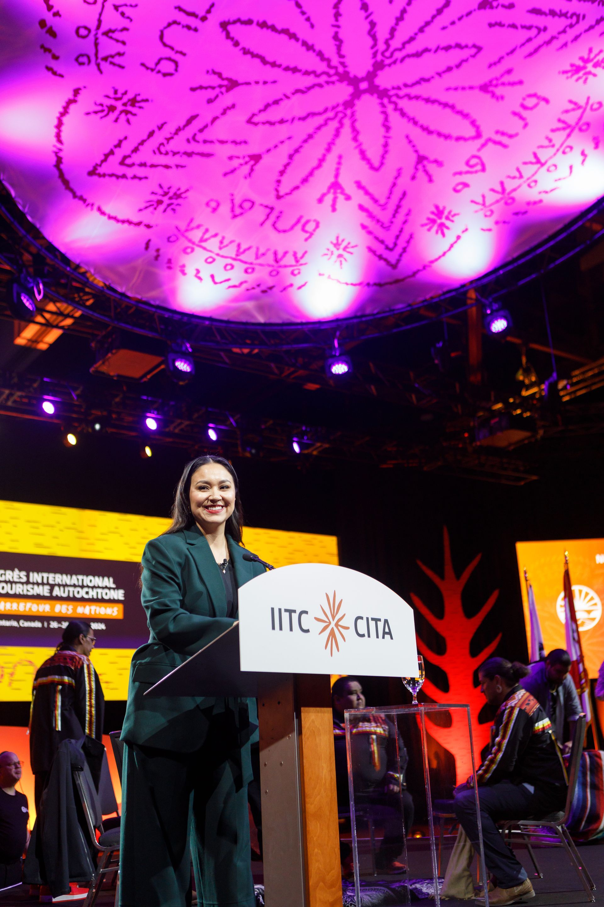 Woman speaking at a podium, illuminated ceiling, stage setup for an event.