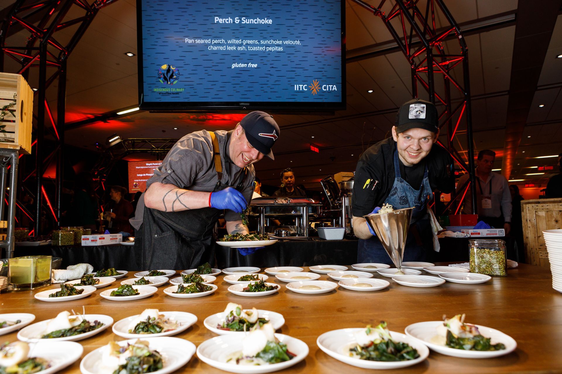 Two men are preparing food on a table with plates of food.