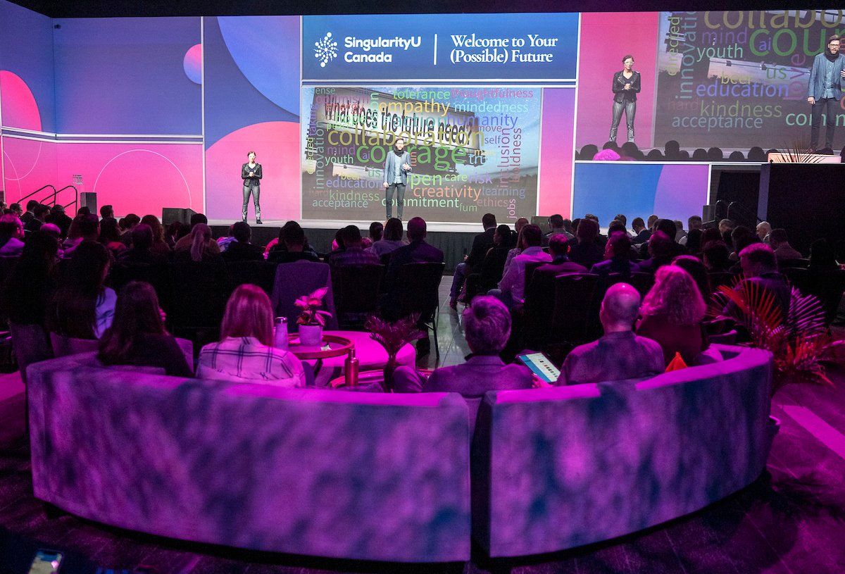 A large group of people are sitting in front of a stage at a conference.