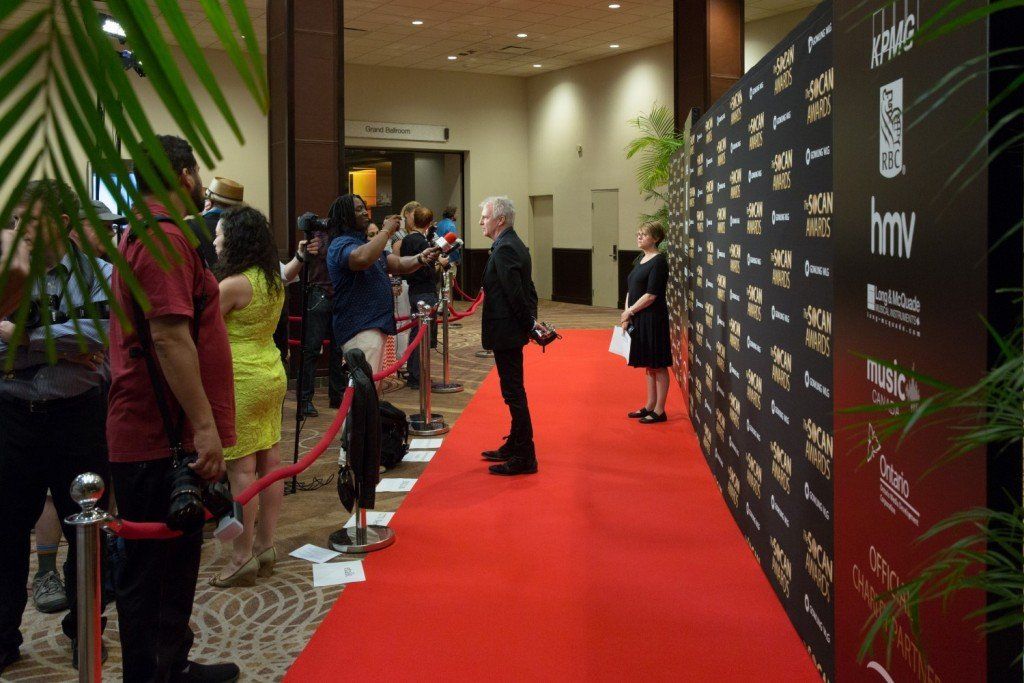 A group of people are standing on a red carpet in a hallway.