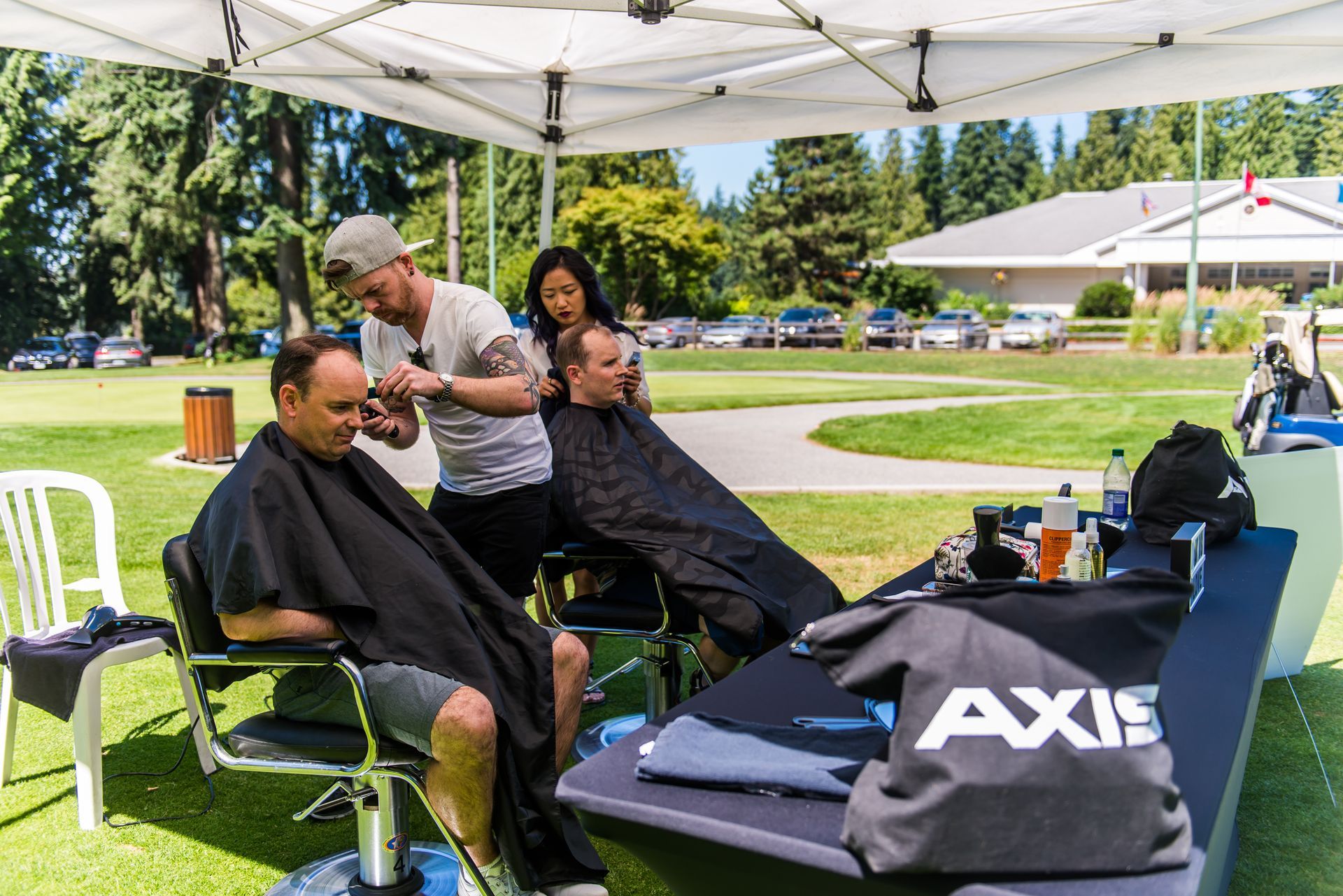 A man is getting his hair cut under a tent in a park.