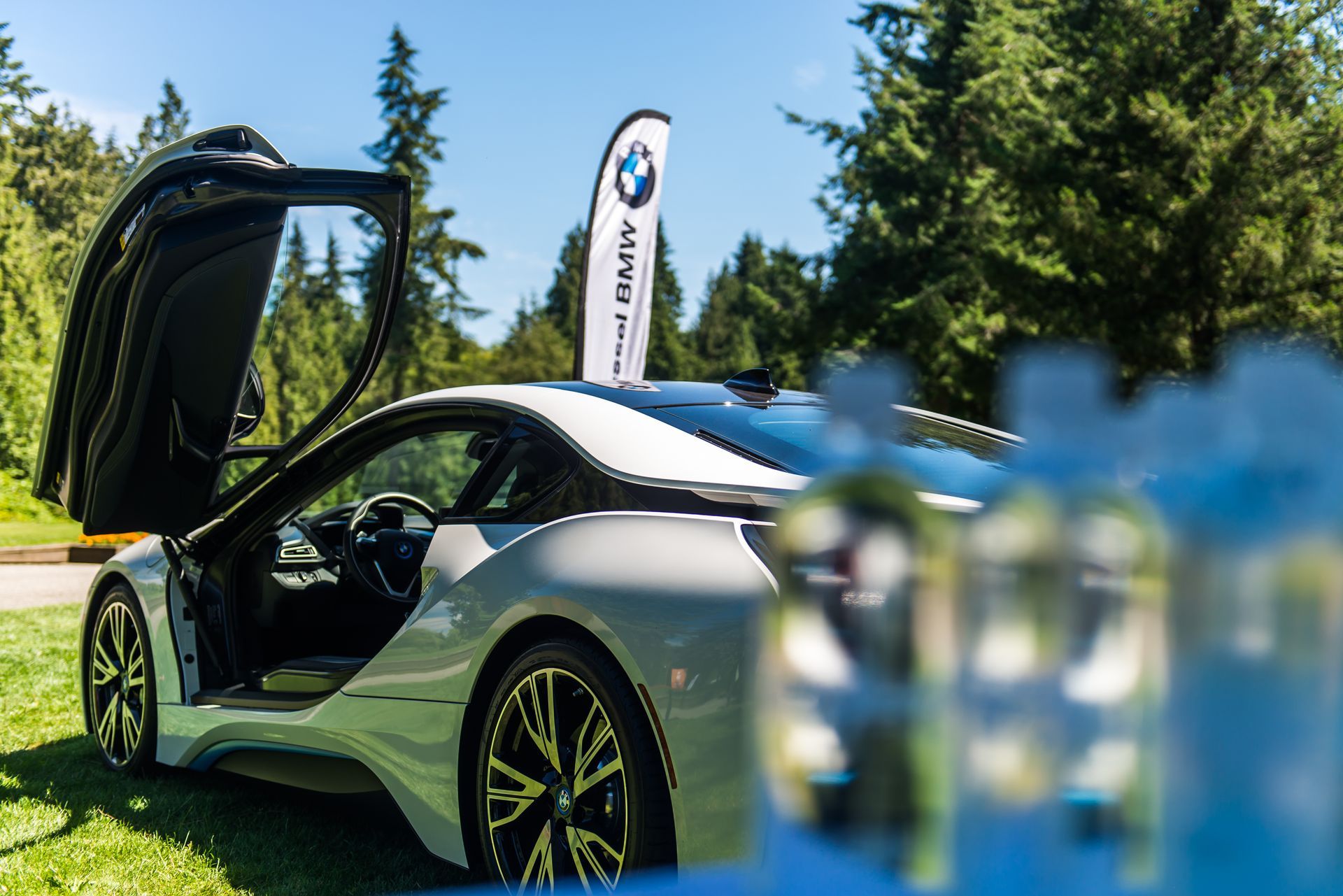 A bmw i8 sports car is parked in the grass with its door open.