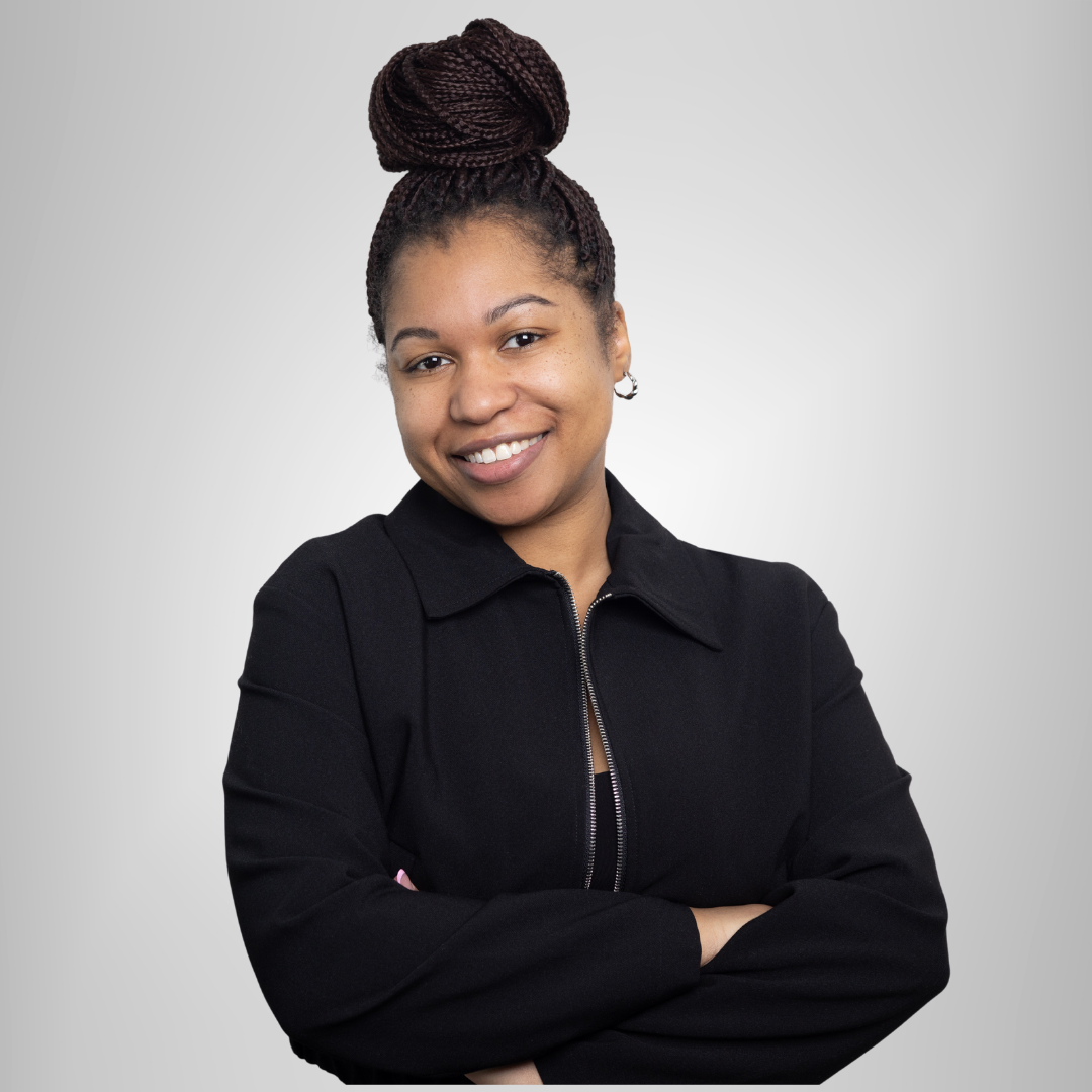 A woman in a black jacket is smiling with her arms crossed