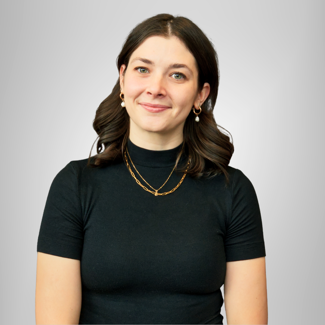 A woman in a pink top and black jeans is smiling.