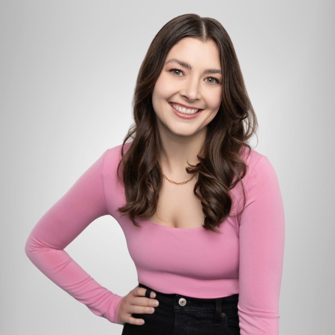 A woman in a pink top and black jeans is smiling.