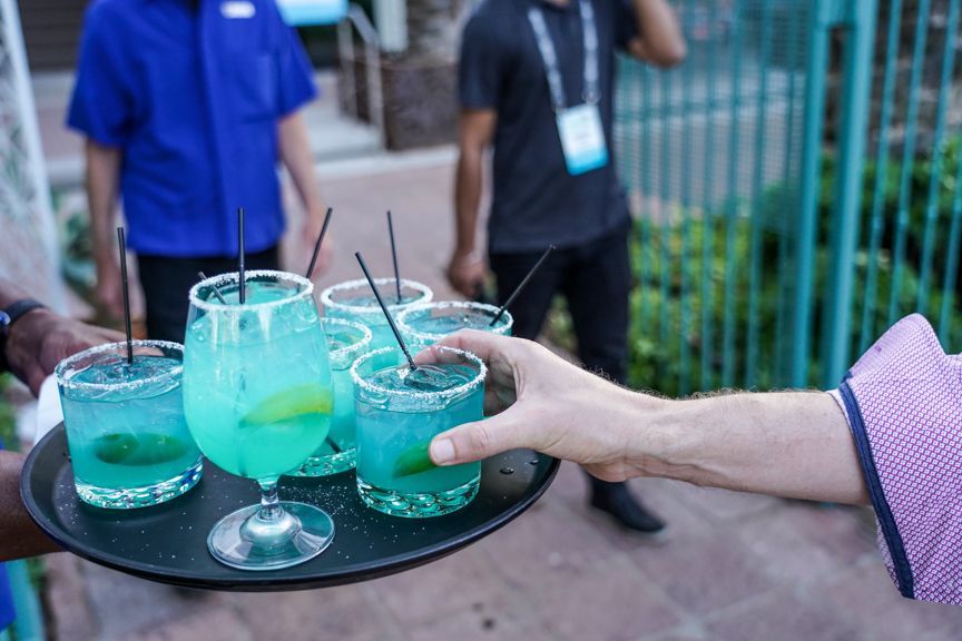 A person is holding a tray of blue drinks.