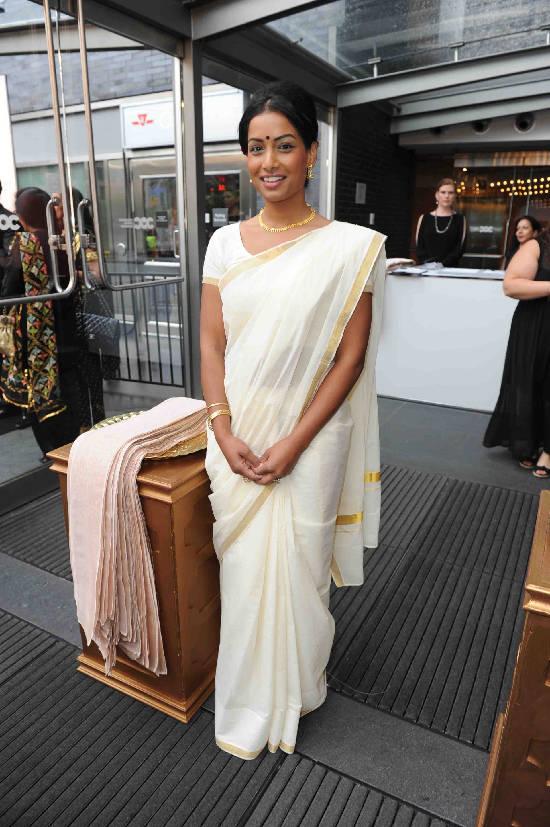 A woman in a white saree is standing in front of a counter.
