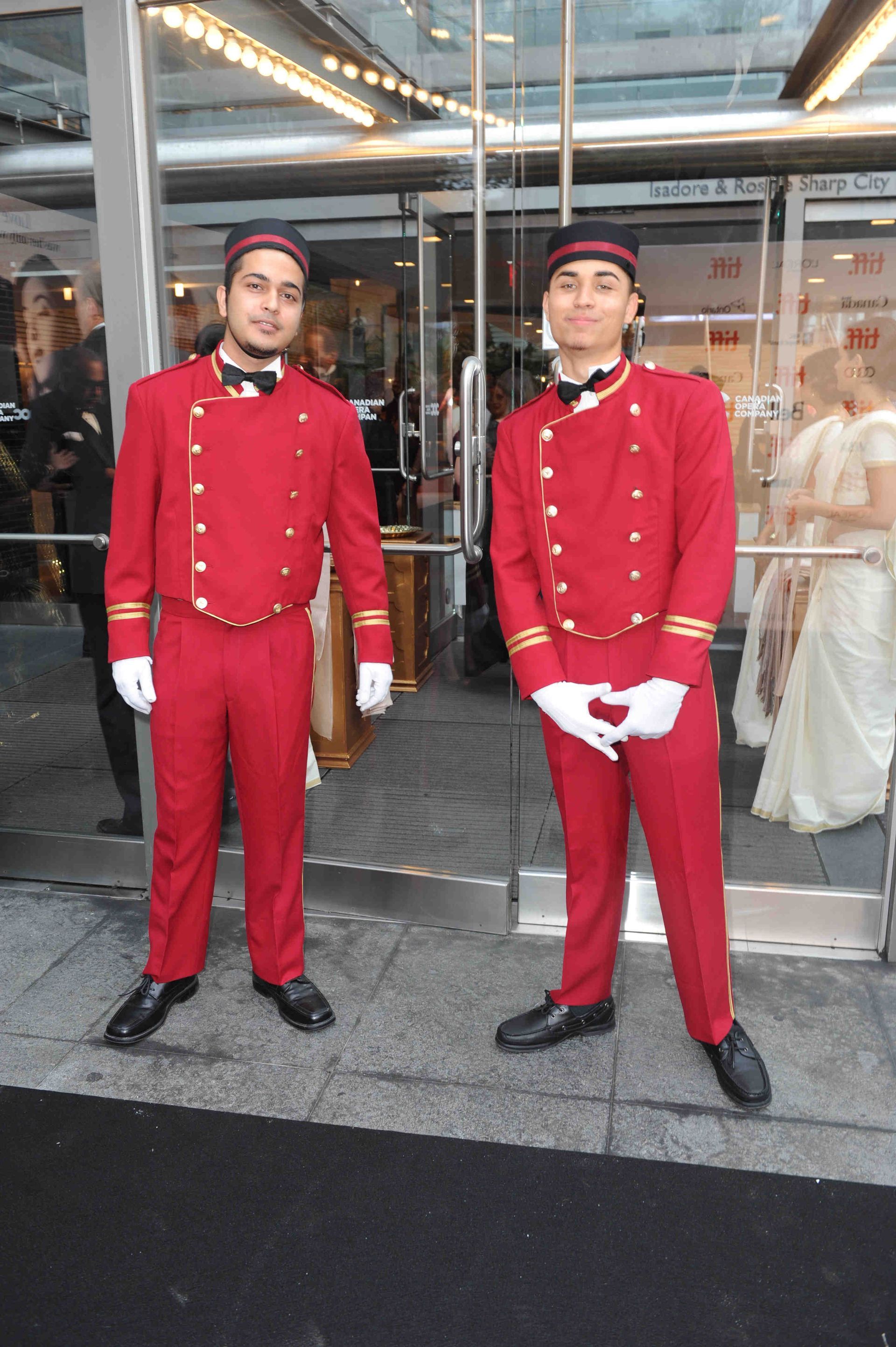 Two men in red uniforms stand in front of a glass door