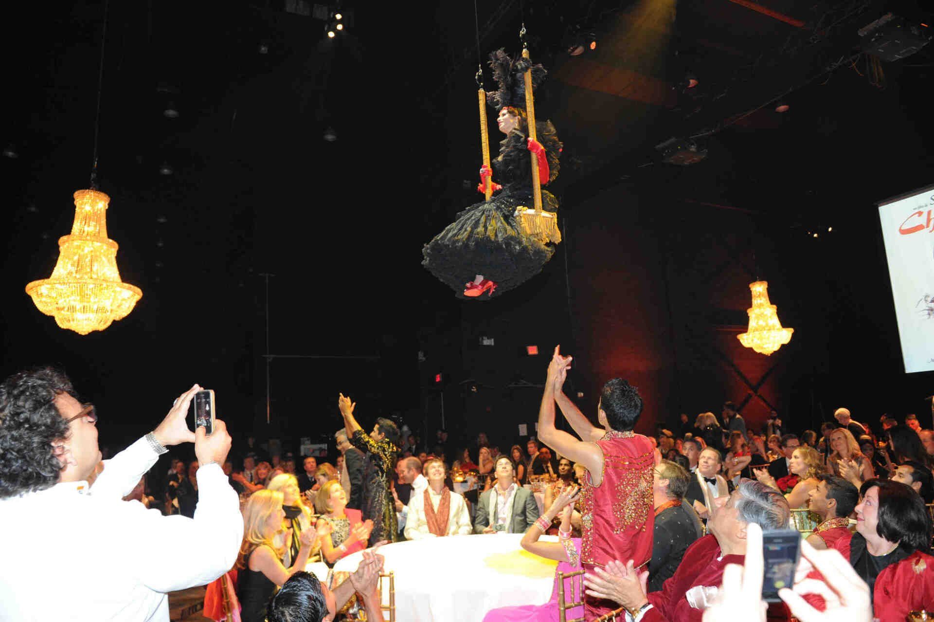 A man is taking a picture of a woman on a trapeze in front of a crowd.