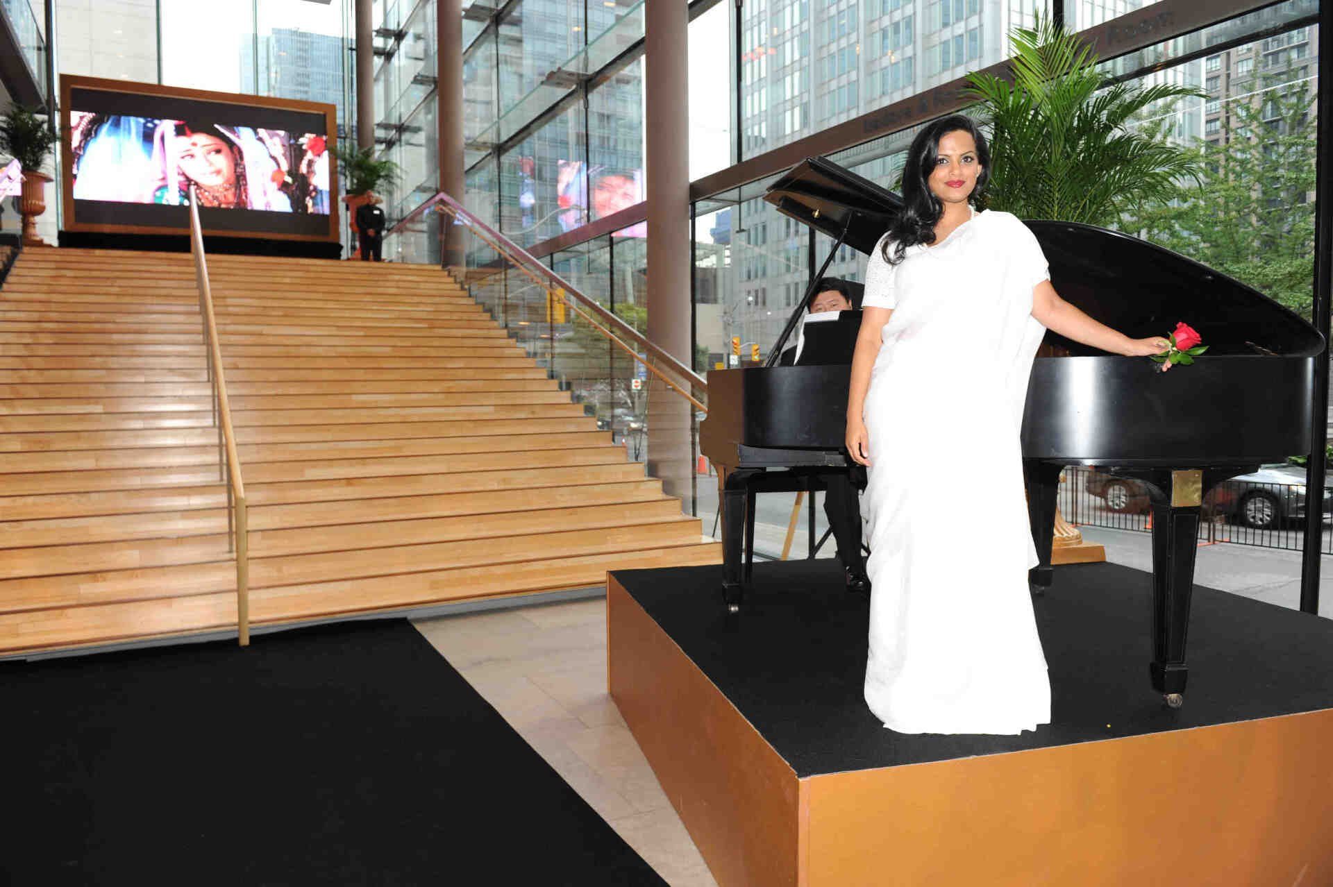 A woman in a white dress is standing in front of a piano.