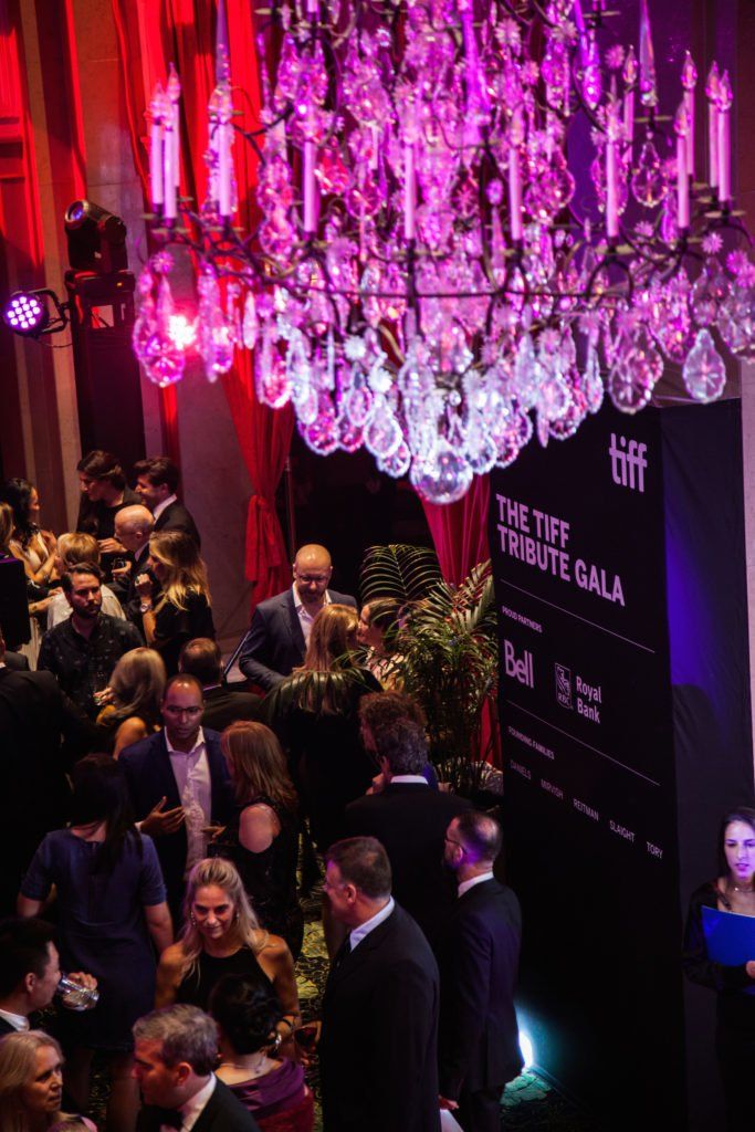 A crowd of people are gathered in a room with a large chandelier.