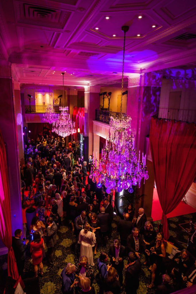 A large crowd of people are gathered in a large room with purple lights.