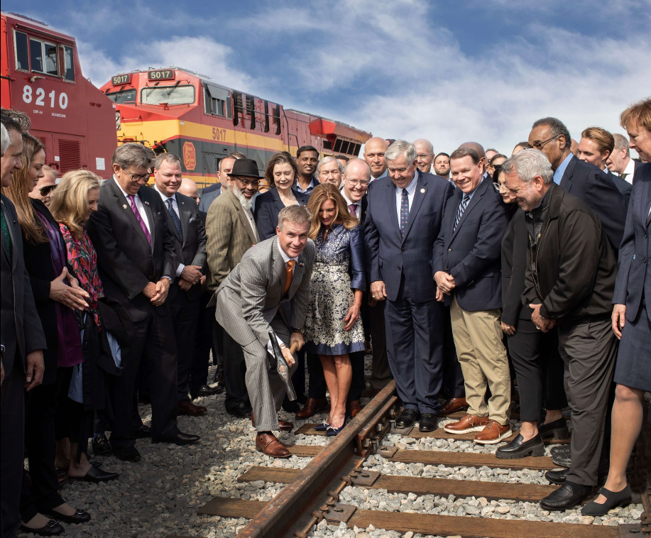 A group of people are standing on train tracks in front of a train numbered 8210