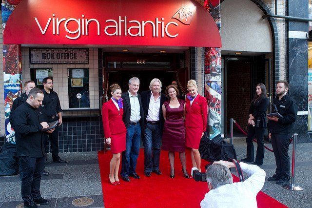 A group of people standing on a red carpet in front of virgin atlantic