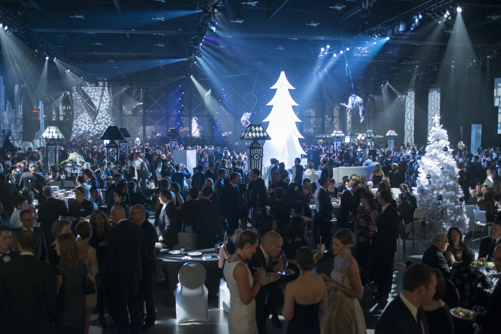 A crowd of people are gathered in a large room with a christmas tree in the middle