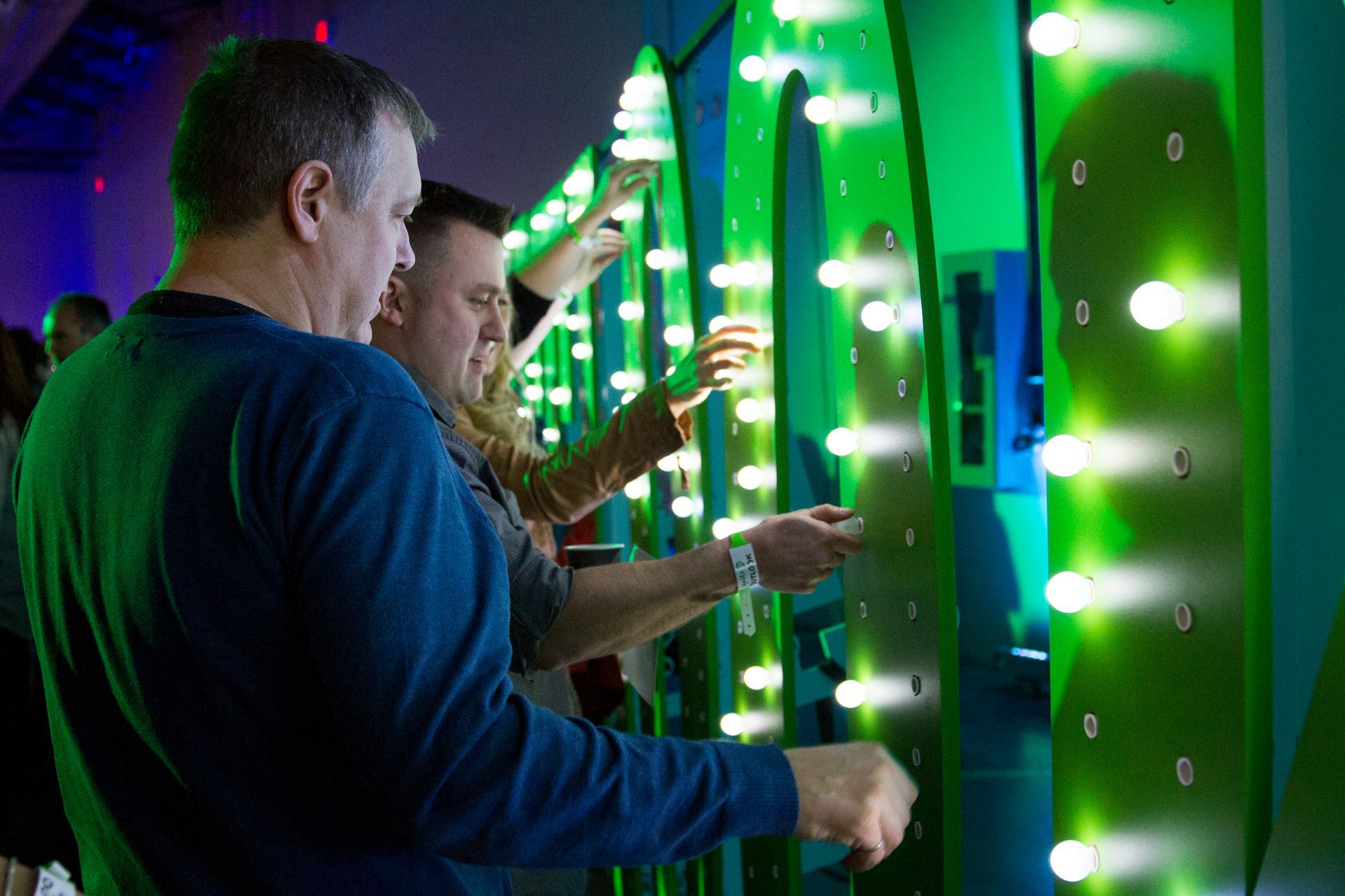 A group of people are standing in front of a wall with green lights on it.