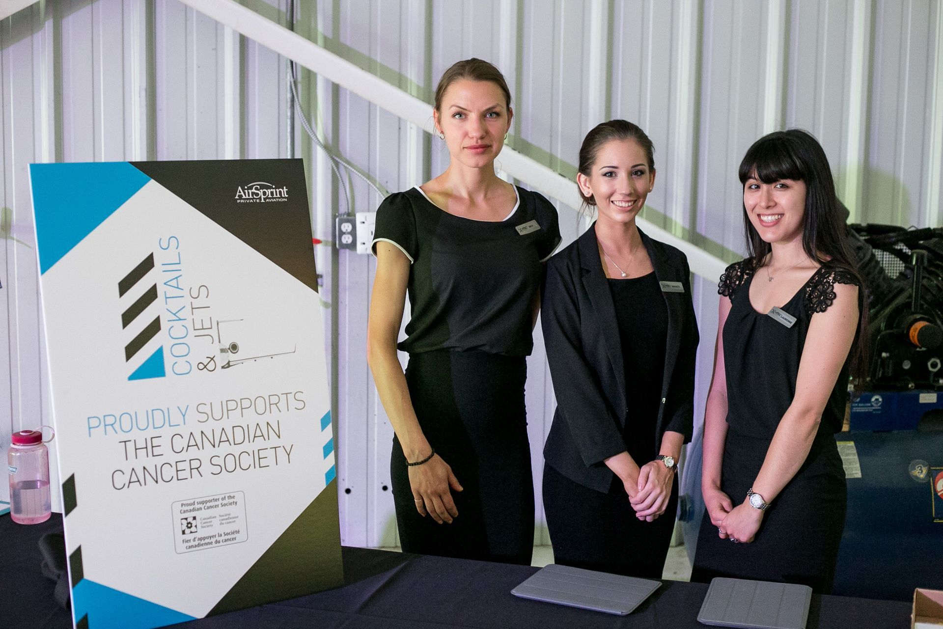 Three women standing in front of a sign that says proudly supports the canadian cancer society