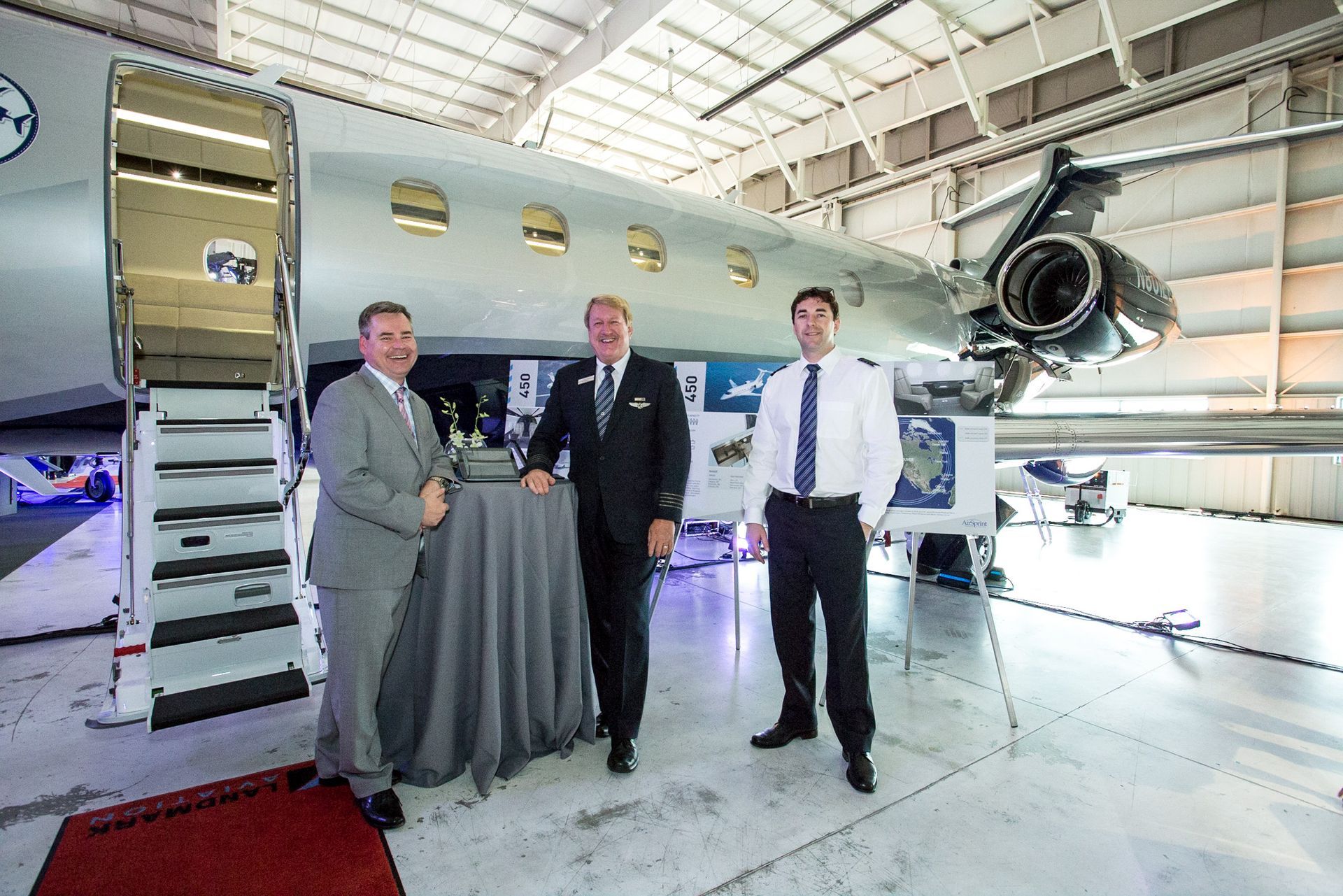 Three men are standing in front of a plane in a hangar.