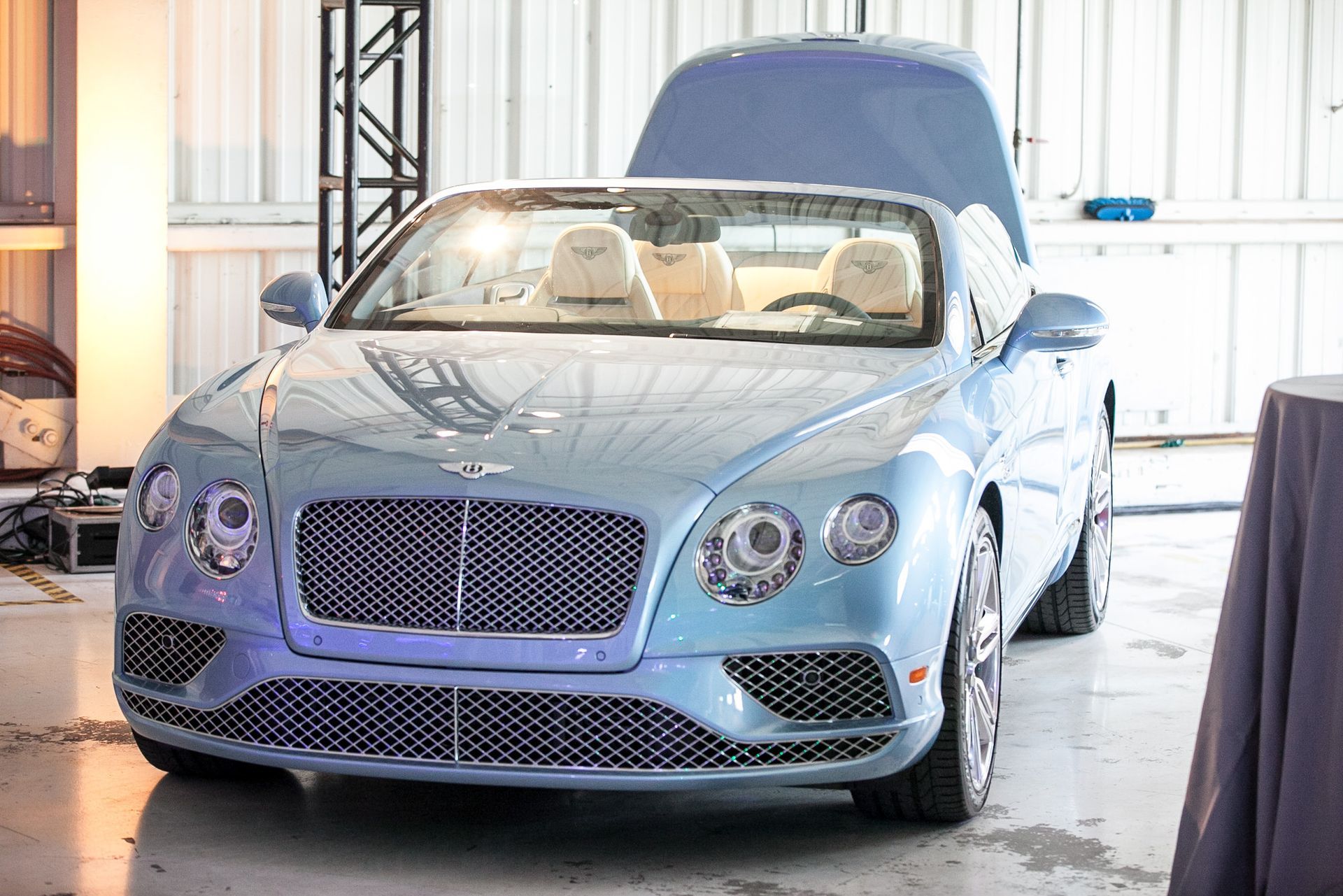 A blue bentley convertible is parked in a garage with its hood open.