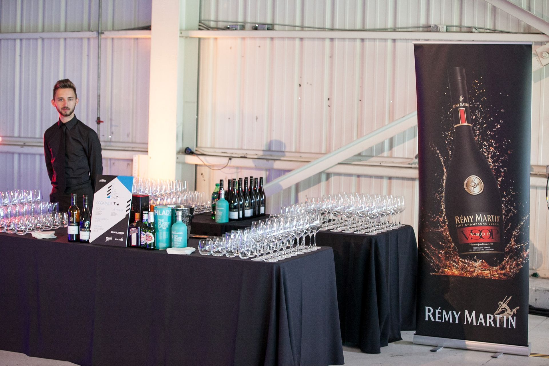 A man is standing in front of a table filled with wine glasses and bottles.