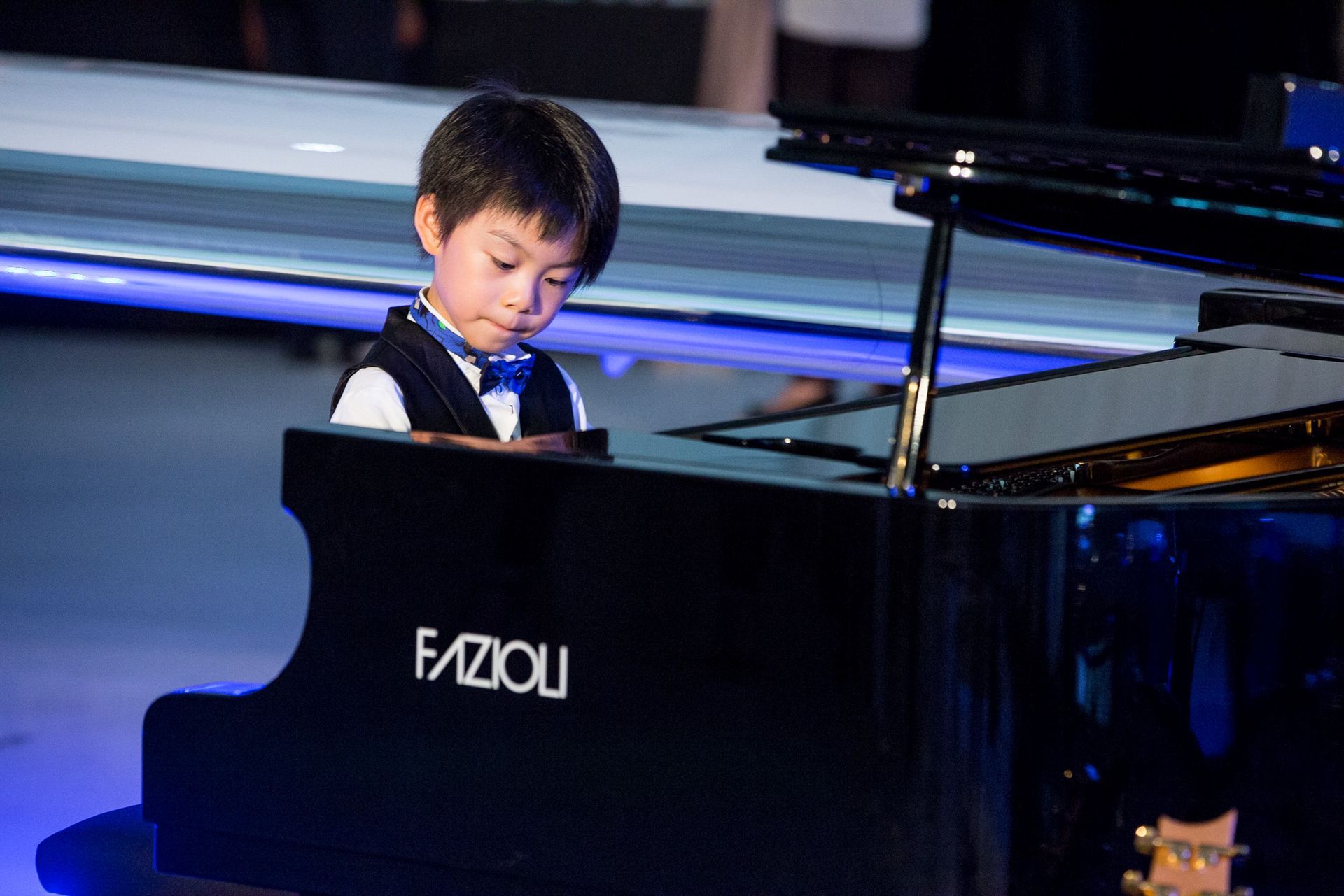 A young boy is playing a black fazioli piano