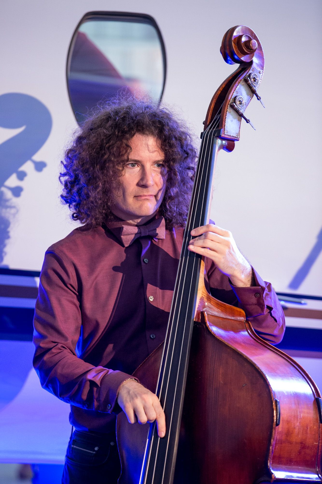 A man with curly hair is playing a double bass.