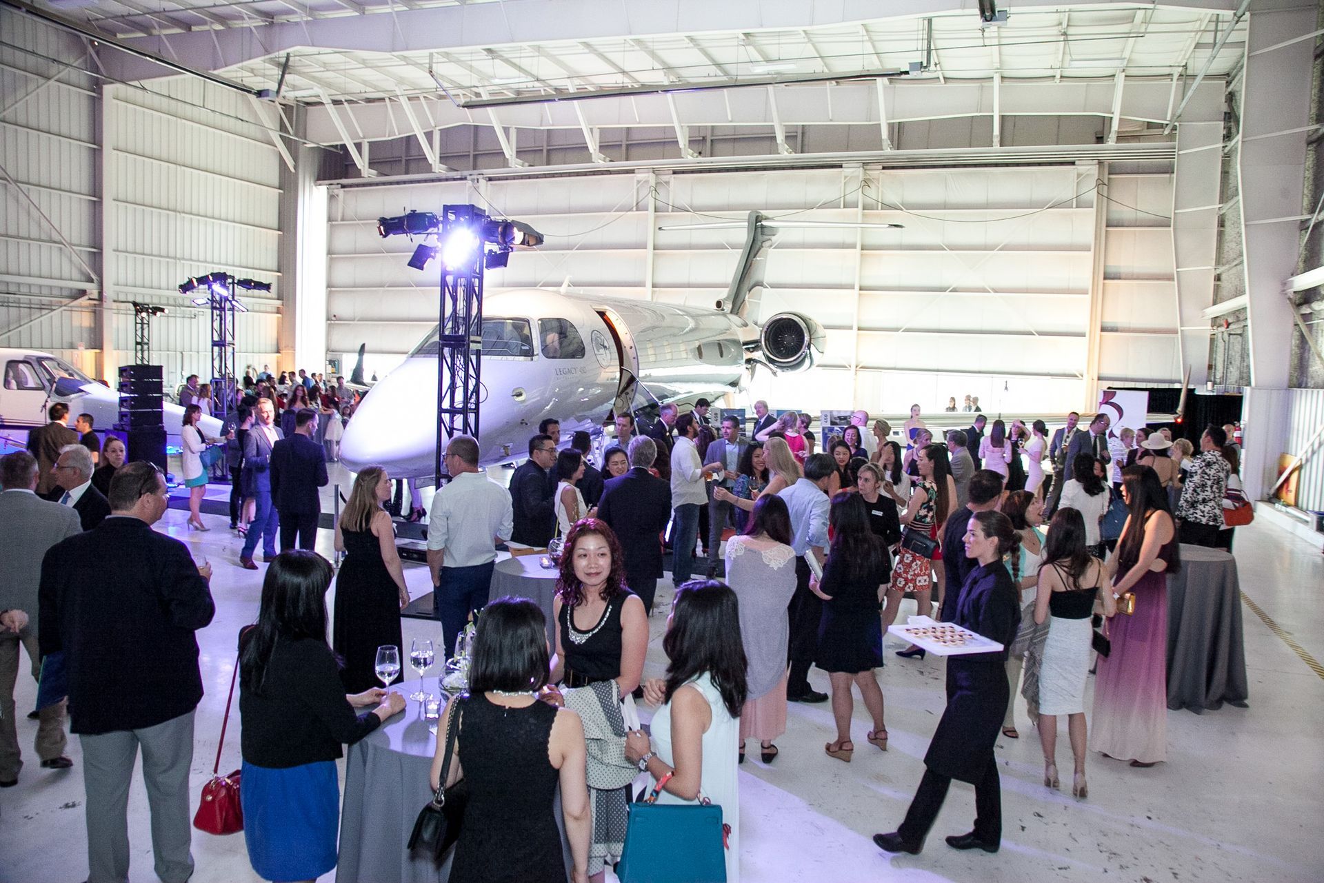 A large group of people are gathered in a hangar with a plane in the background.