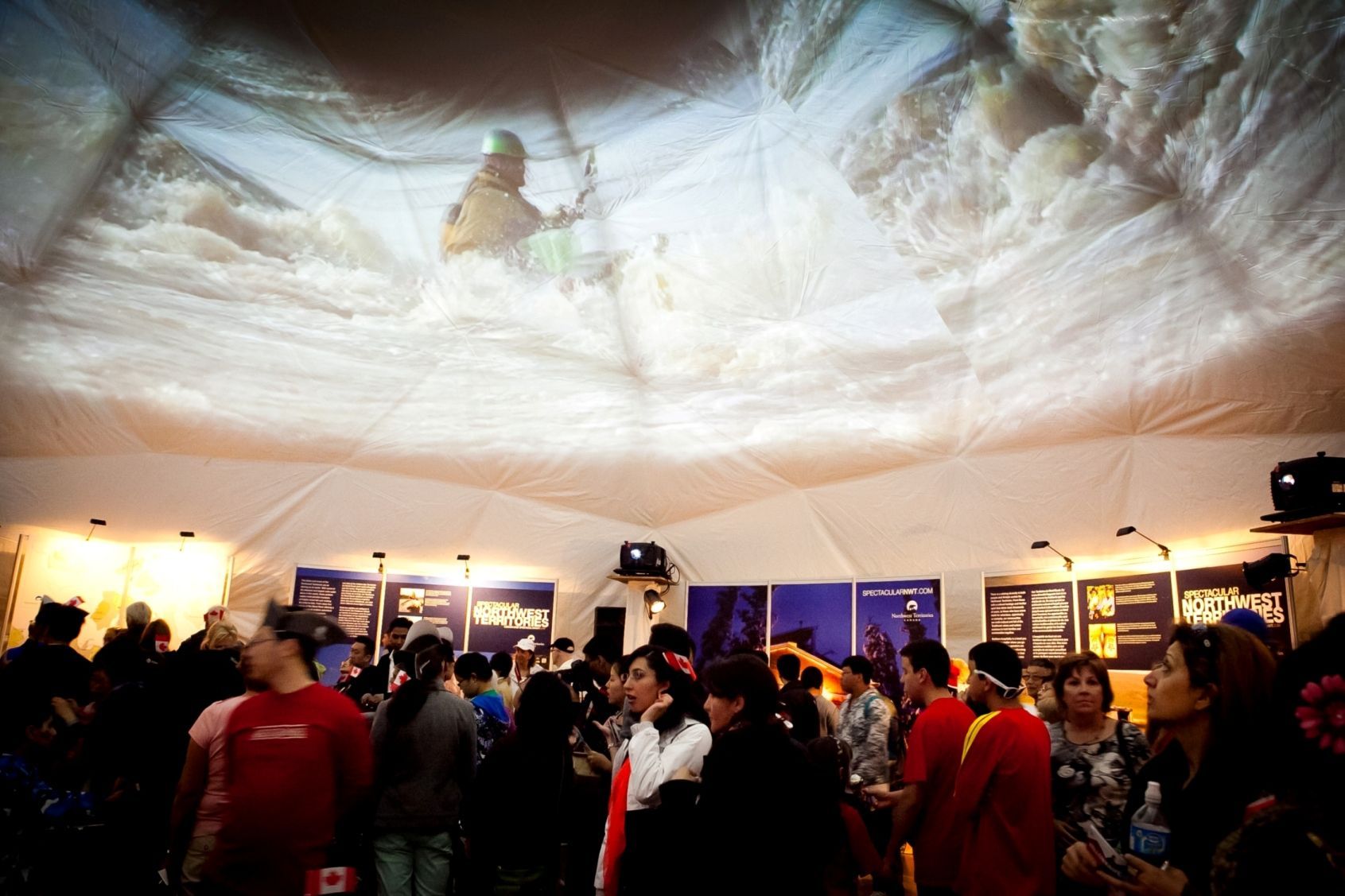 People inside a tent watching a video projected on the ceiling of a kayaker in whitewater.